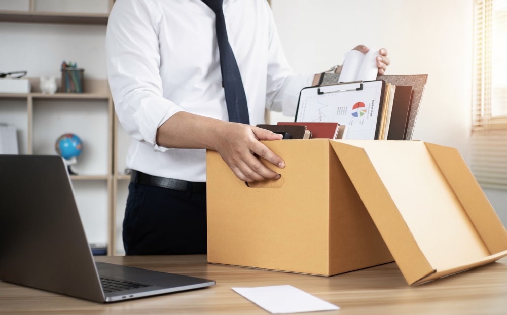 Office worker packing belongings after termination linked to criminal charges and employment in Canada.